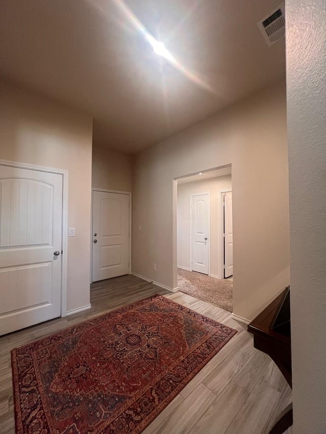 hall with visible vents, baseboards, and wood finished floors