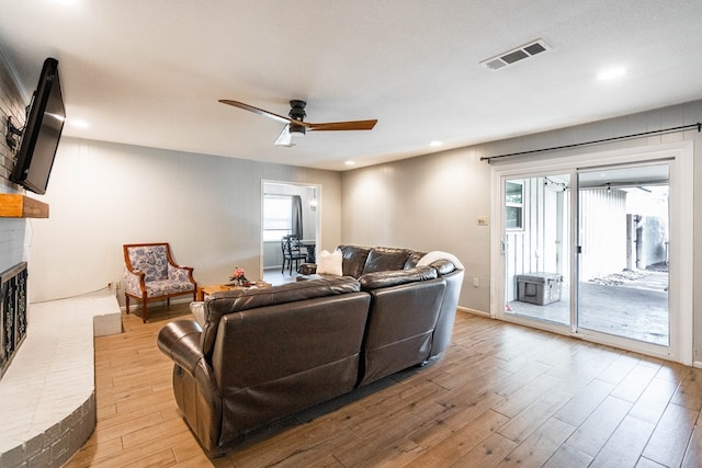 living room with a ceiling fan, visible vents, a brick fireplace, light wood-type flooring, and recessed lighting