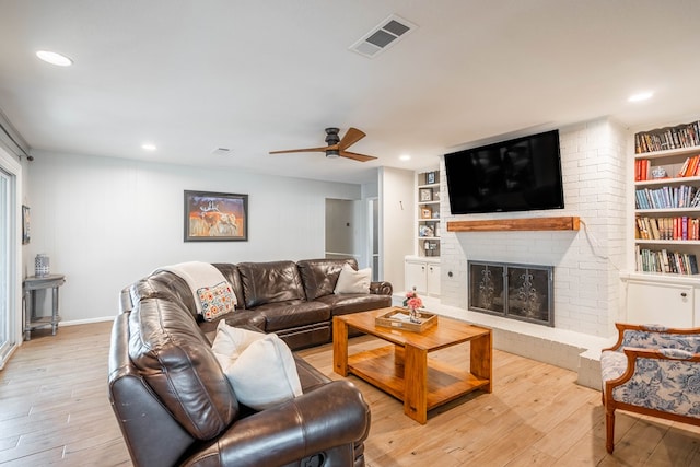 living area featuring visible vents, a brick fireplace, built in shelves, and light wood-type flooring