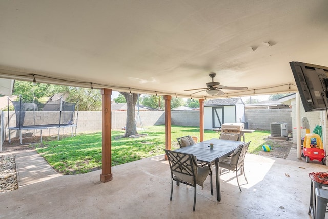 view of patio with cooling unit, outdoor dining area, a fenced backyard, a trampoline, and a storage shed