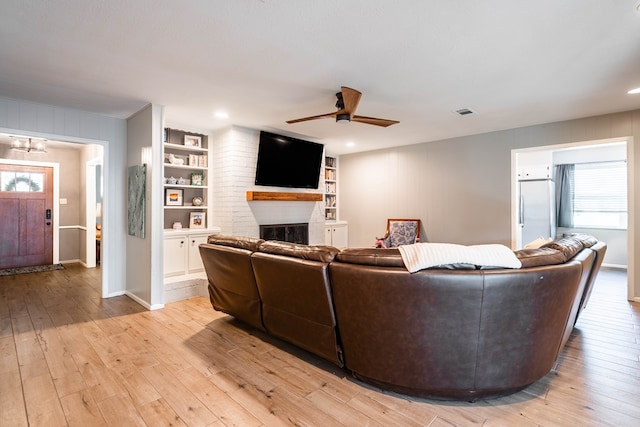 living room featuring visible vents, a brick fireplace, light wood-style floors, ceiling fan with notable chandelier, and a wealth of natural light