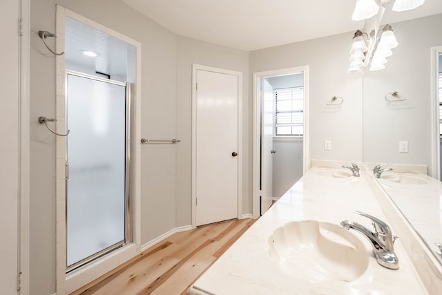 full bath featuring double vanity, a sink, a shower stall, and wood finished floors