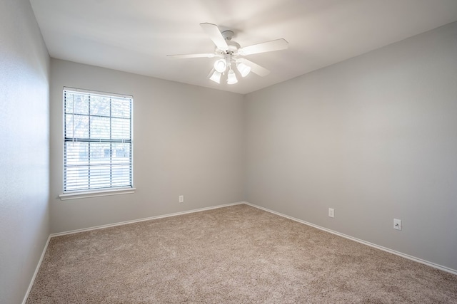 carpeted spare room with a ceiling fan and baseboards