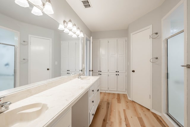 bathroom with double vanity, visible vents, a stall shower, a sink, and wood finished floors