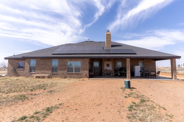 rear view of house featuring brick siding, a chimney, a patio area, and roof mounted solar panels