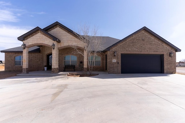 french country inspired facade with a garage, driveway, brick siding, and stone siding