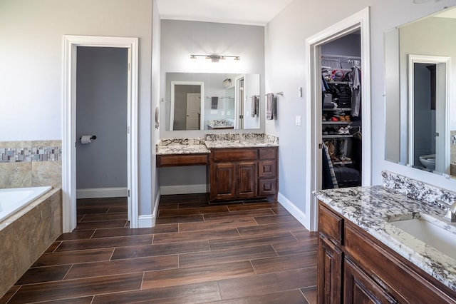 full bath featuring wood tiled floor, a walk in closet, two vanities, and a sink