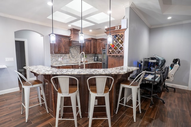 kitchen with tasteful backsplash, arched walkways, wood finish floors, and a large island with sink