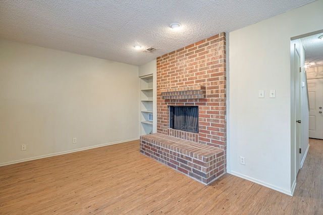 unfurnished living room featuring a fireplace, built in features, light hardwood / wood-style flooring, and a textured ceiling