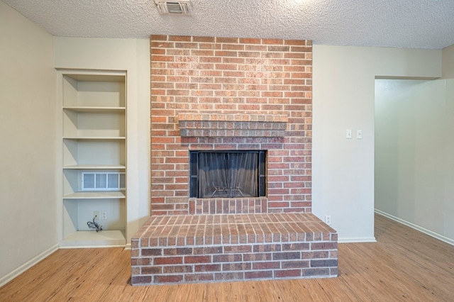 unfurnished living room featuring a fireplace, built in features, hardwood / wood-style floors, and a textured ceiling