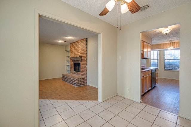 kitchen with a fireplace, black dishwasher, a textured ceiling, and light hardwood / wood-style flooring