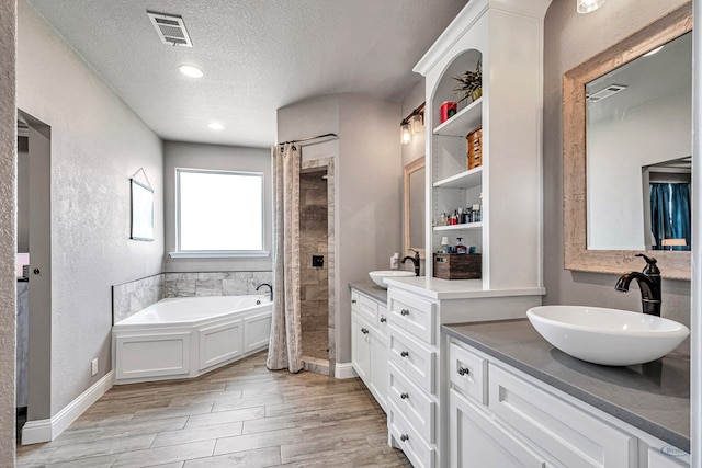6811 W County Rd 41, Midland, TX 79707 - full bathroom with a shower stall, a textured ceiling, a garden tub, vanity, and wood finished floors