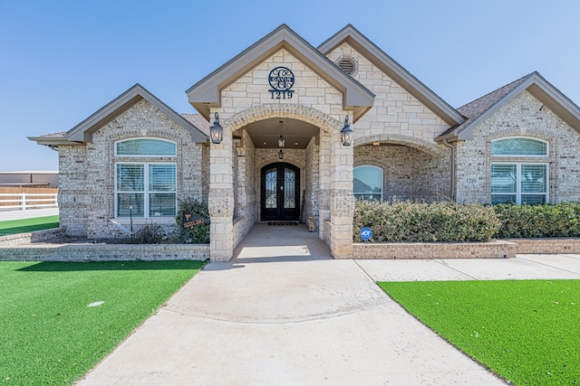 doorway to property featuring brick siding, a yard, and french doors