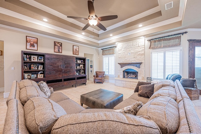 living area featuring a tray ceiling, visible vents, ornamental molding, ceiling fan, and a stone fireplace