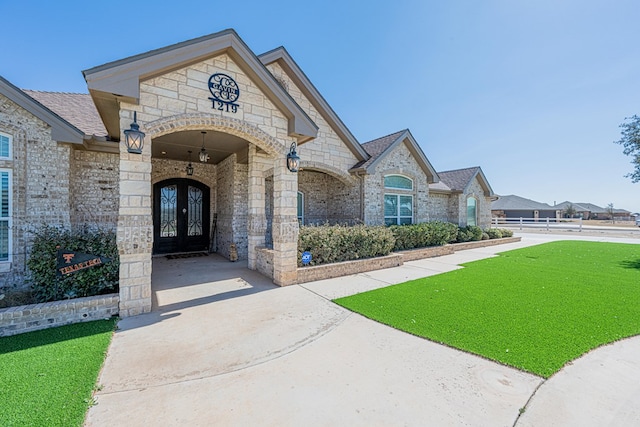 french country inspired facade with stone siding, a front yard, brick siding, and french doors