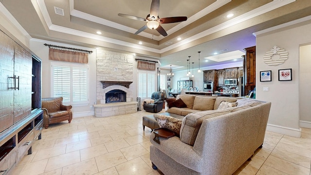 living room with visible vents, a tray ceiling, ornamental molding, and a stone fireplace