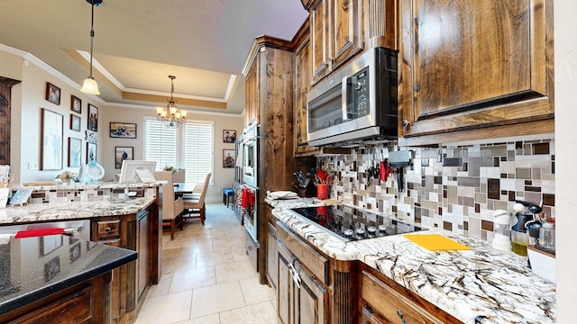 kitchen with a chandelier, appliances with stainless steel finishes, decorative backsplash, a tray ceiling, and crown molding