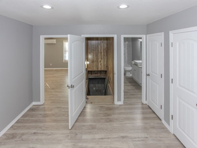 hallway with light wood-type flooring, recessed lighting, a wall unit AC, and baseboards