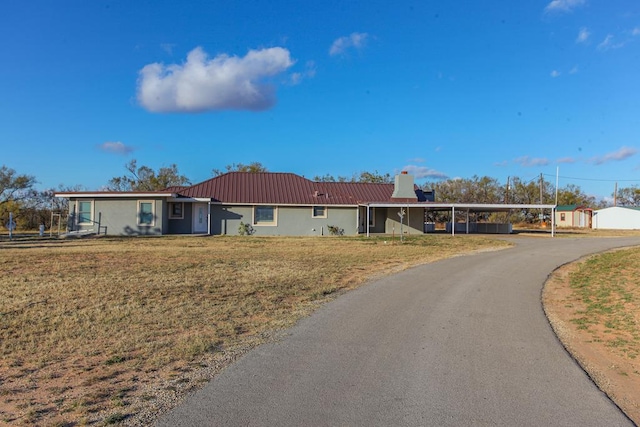 ranch-style house with metal roof, a carport, a chimney, and a front yard