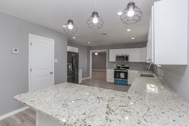 kitchen featuring appliances with stainless steel finishes, light wood-type flooring, white cabinetry, pendant lighting, and a sink