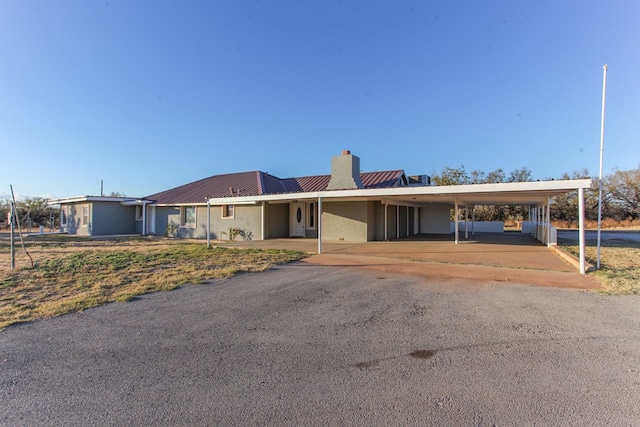 view of front facade with metal roof, an attached carport, driveway, stucco siding, and a chimney