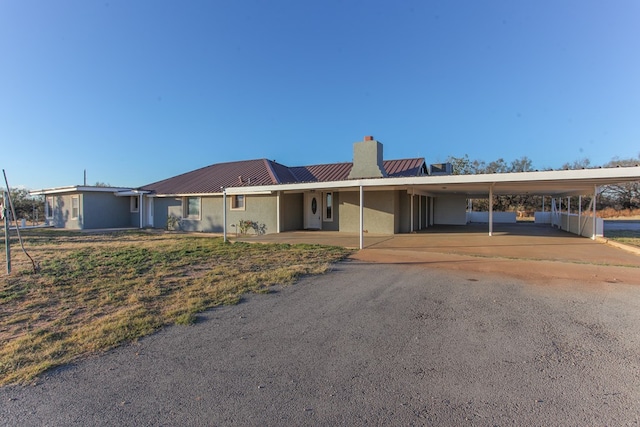 ranch-style house with driveway, an attached carport, metal roof, and a chimney