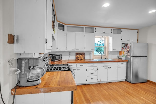 kitchen with a sink, appliances with stainless steel finishes, butcher block countertops, white cabinets, and recessed lighting