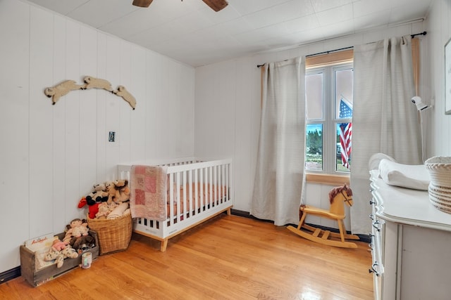 bedroom with light wood finished floors, a crib, and a ceiling fan