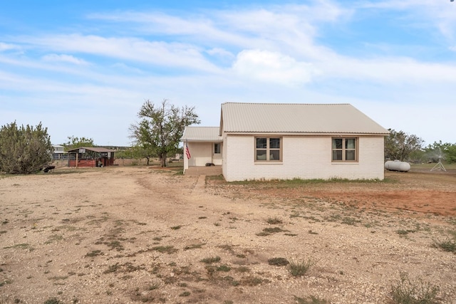 view of home's exterior featuring brick siding, metal roof, and dirt driveway