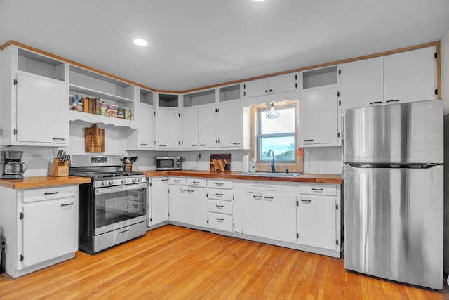 kitchen featuring stainless steel appliances, a sink, open shelves, white cabinets, and light wood-style flooring