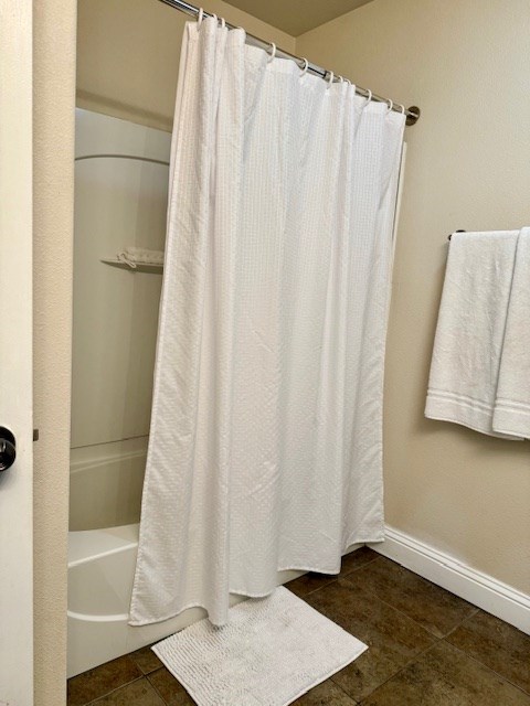 bathroom with tile patterned flooring, baseboards, and shower / bathtub combination with curtain