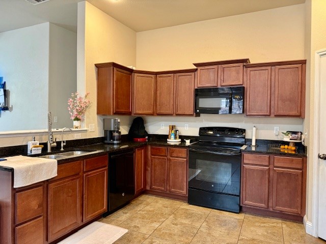 kitchen with visible vents, a sink, light tile patterned floors, black appliances, and dark stone counters