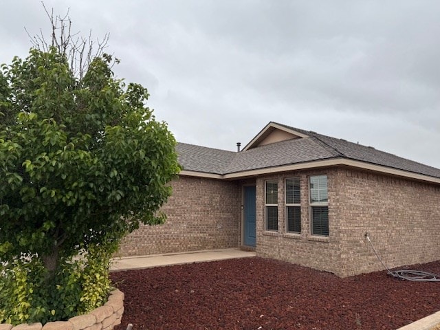 view of side of home featuring brick siding, a shingled roof, and a patio