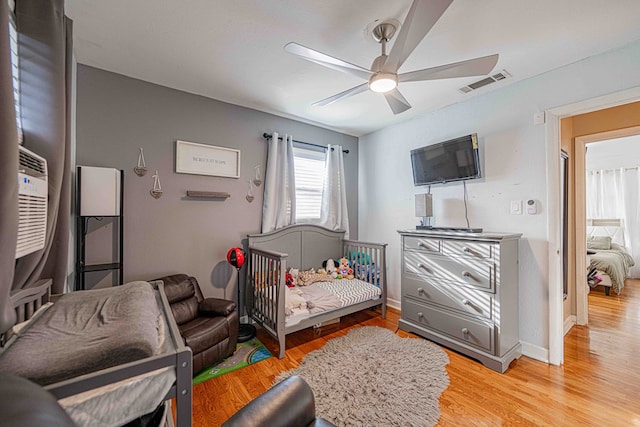 bedroom featuring ceiling fan, light hardwood / wood-style floors, and a nursery area