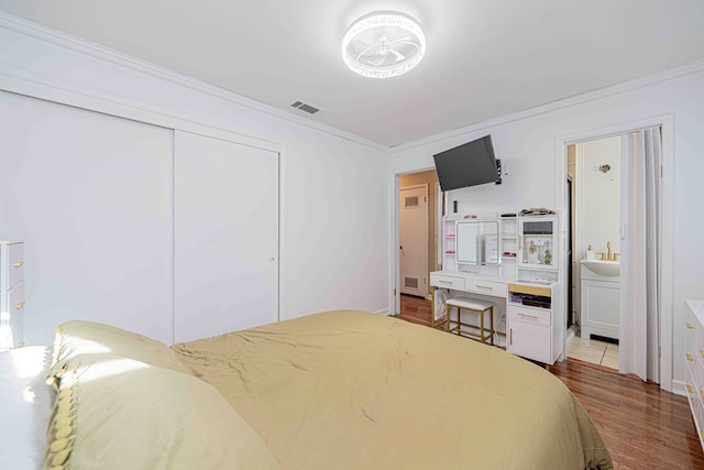 bedroom featuring hardwood / wood-style flooring, crown molding, connected bathroom, and a closet