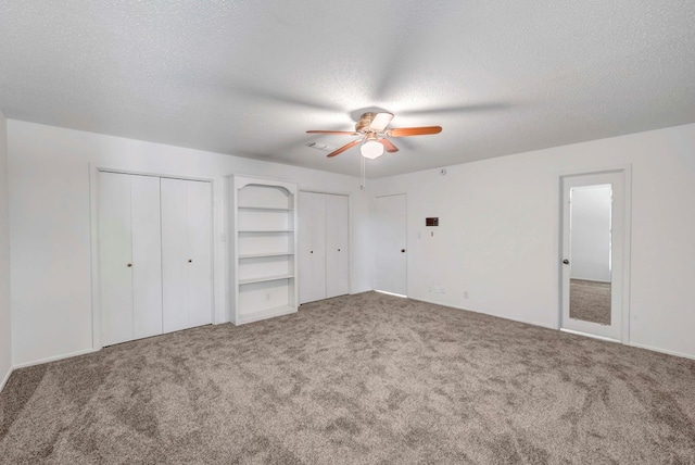 unfurnished bedroom with ceiling fan, two closets, carpet floors, and a textured ceiling