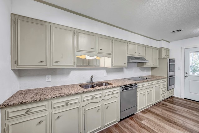 kitchen with appliances with stainless steel finishes, hardwood / wood-style floors, sink, light stone counters, and a textured ceiling