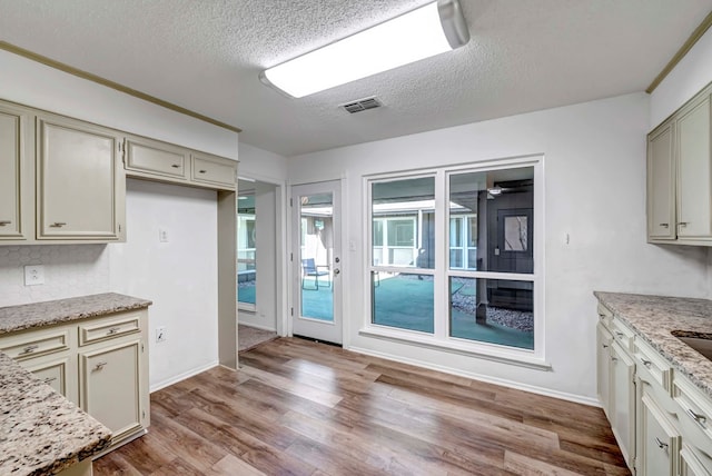 kitchen featuring light stone counters, light hardwood / wood-style flooring, cream cabinetry, and a textured ceiling