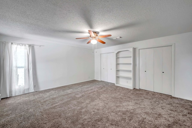 unfurnished bedroom with multiple closets, ceiling fan, carpet floors, and a textured ceiling