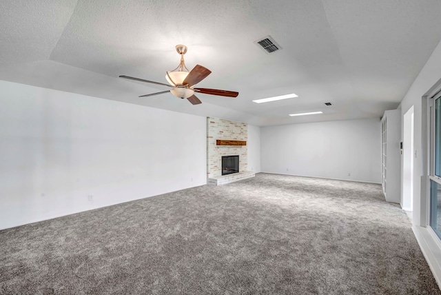 unfurnished living room featuring ceiling fan, carpet flooring, a brick fireplace, and a textured ceiling