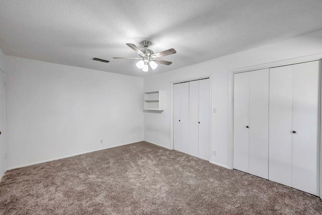 unfurnished bedroom featuring multiple closets, ceiling fan, carpet, and a textured ceiling