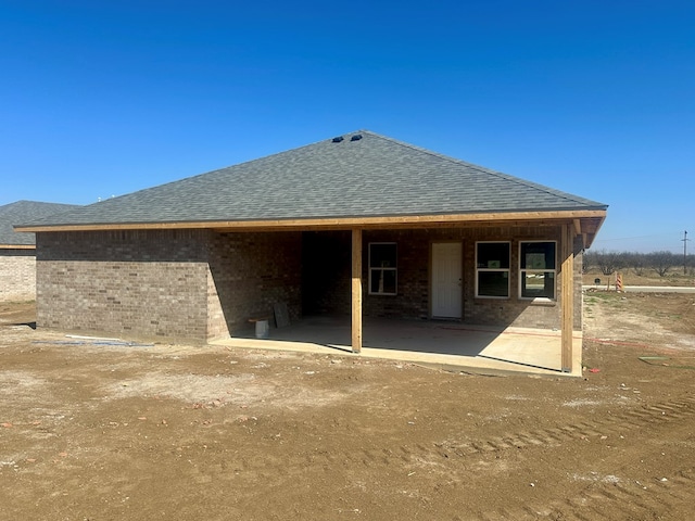 rear view of property with a shingled roof and brick siding