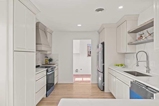 kitchen featuring sink, white cabinetry, tasteful backsplash, premium range hood, and appliances with stainless steel finishes