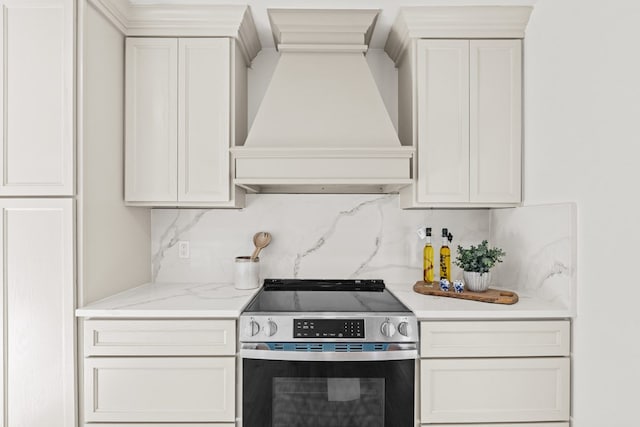 kitchen with white cabinetry, light stone counters, stainless steel electric range oven, backsplash, and premium range hood