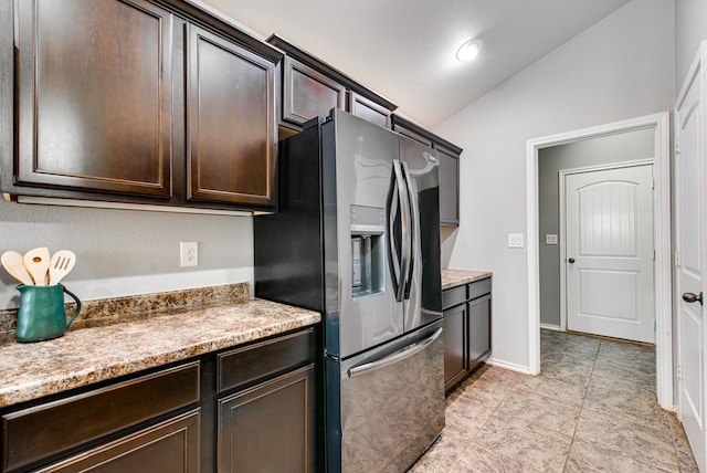 kitchen with lofted ceiling, light tile patterned flooring, dark brown cabinets, stainless steel fridge, and light countertops