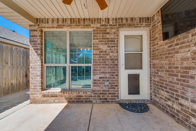 view of exterior entry with fence, a patio, ceiling fan, and brick siding