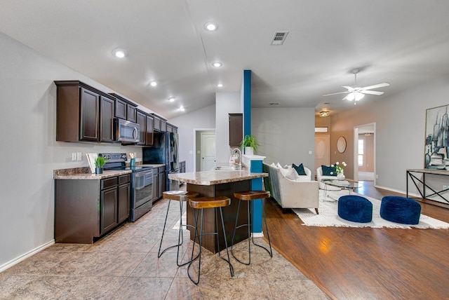 kitchen with dark brown cabinetry, visible vents, a sink, open floor plan, and stainless steel appliances