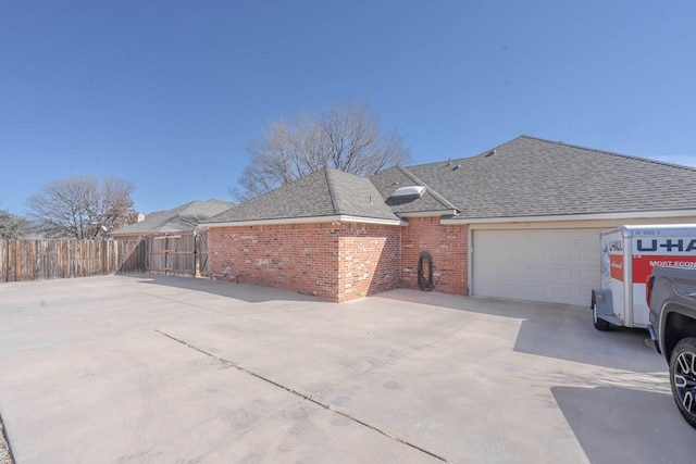 view of property exterior featuring fence, concrete driveway, an attached garage, a shingled roof, and brick siding