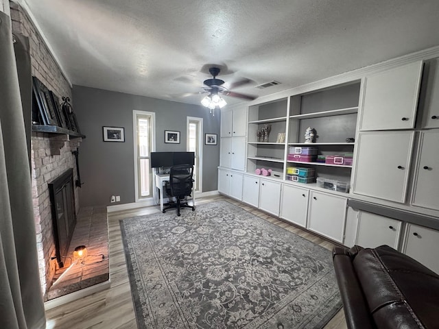 3212 Fannin Ave, Midland, TX 79705 - home office featuring a ceiling fan, light wood-style floors, a textured ceiling, and a brick fireplace