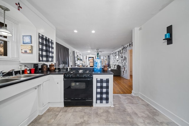 407 Edwards Blvd, Big Spring, TX 79720 - kitchen with black gas range oven, a peninsula, dark countertops, ceiling fan, and white cabinetry
